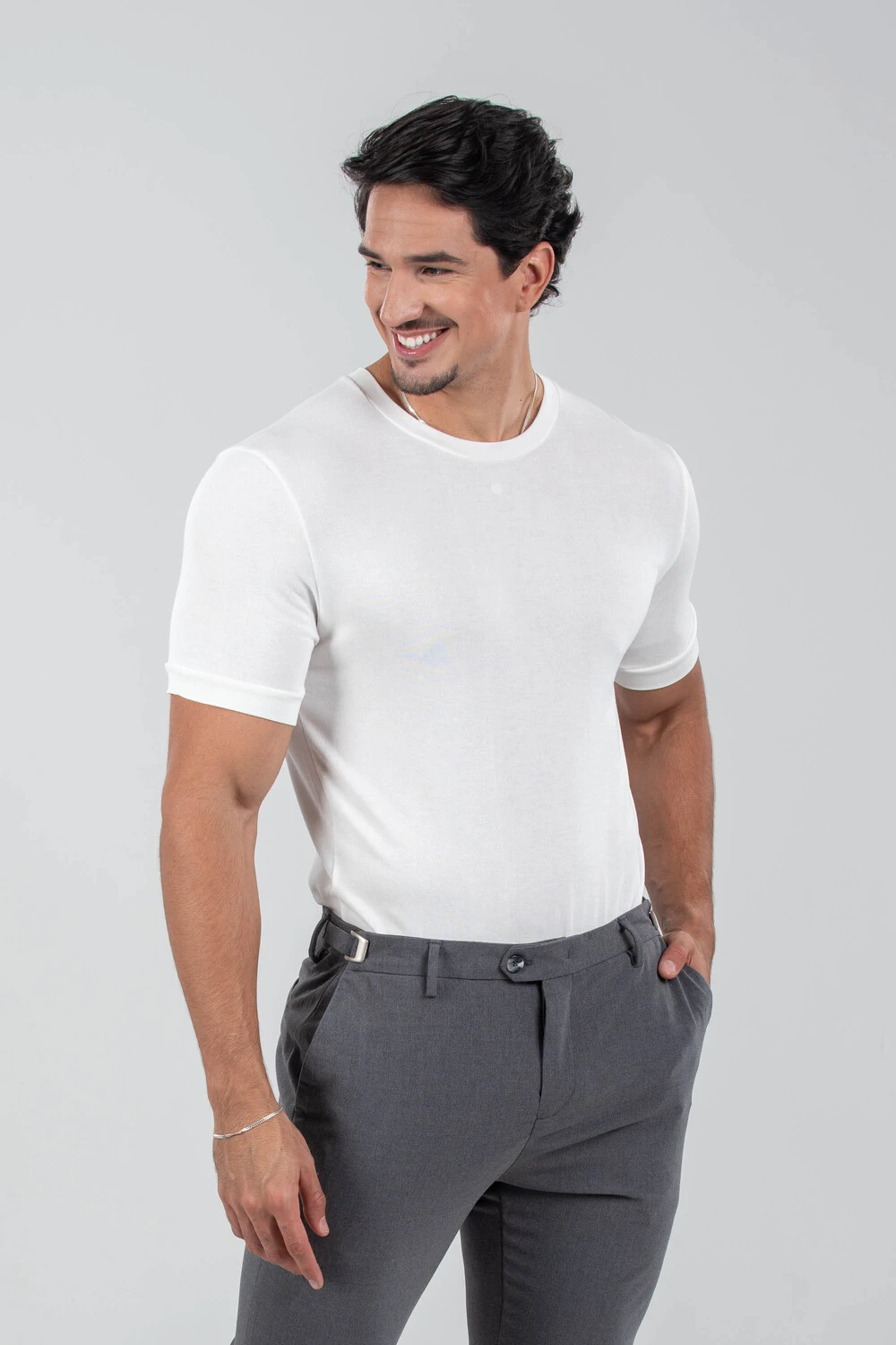 Homem sorrindo com camiseta branca de tricô e calça cinza