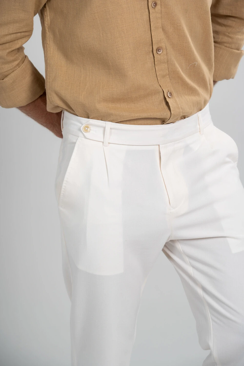 Detalhe de calça de alfaiataria off-white com pregas e cinto marrom
