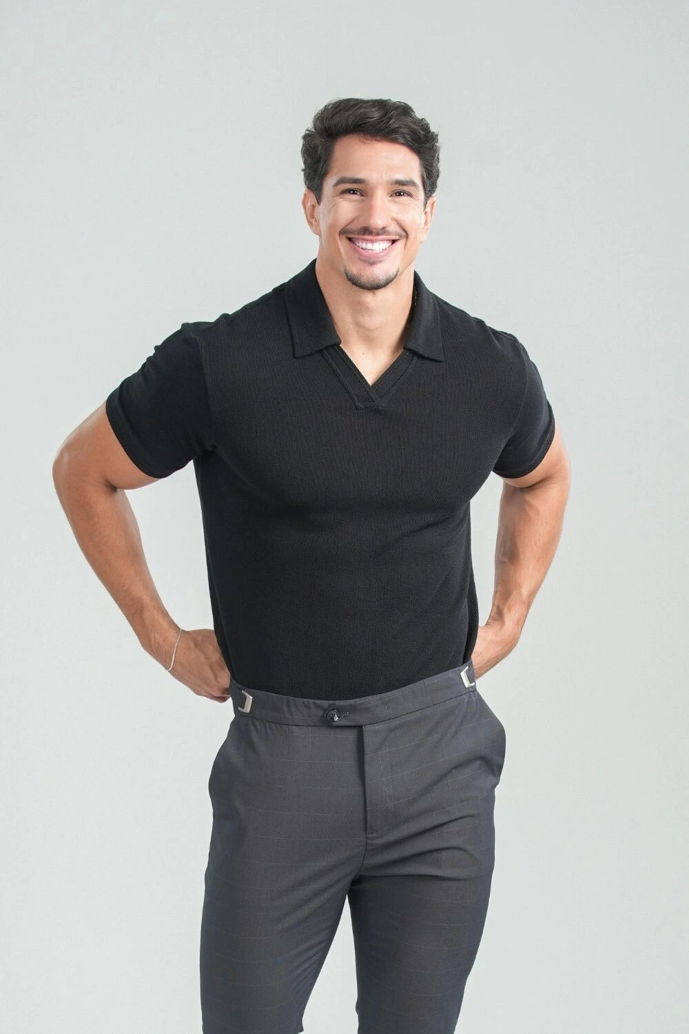 Homem sorrindo com camisa polo de tricô preta sem botão e calça cinza