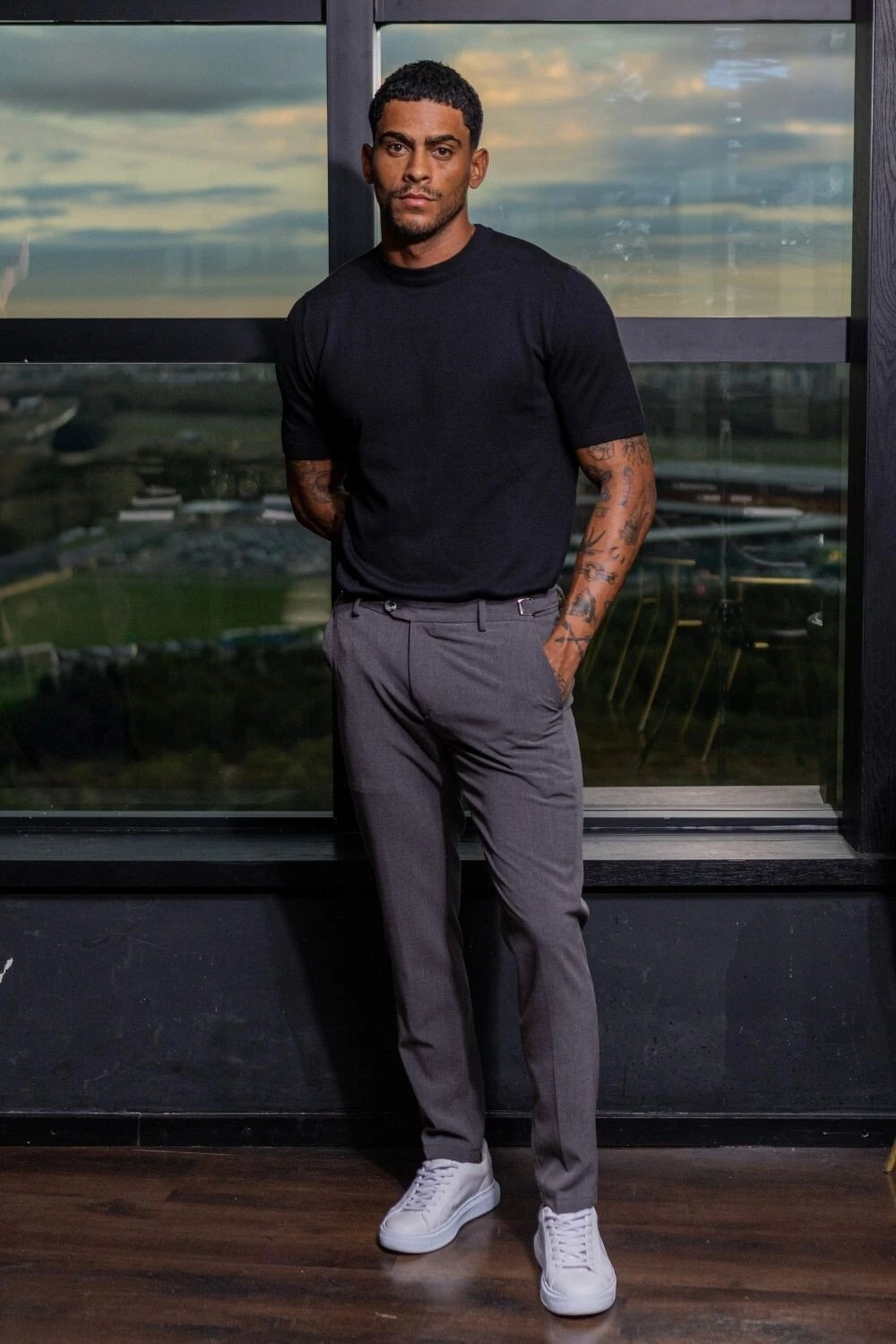 Homem com camiseta preta, calça de alfaiataria cinza e tênis branco, look masculino para viajar