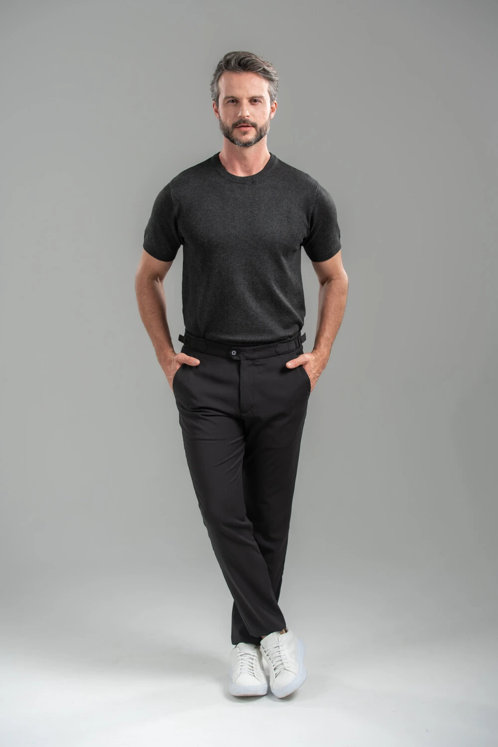 Homem com camiseta preta, calça de alfaiataria escura e tênis branco