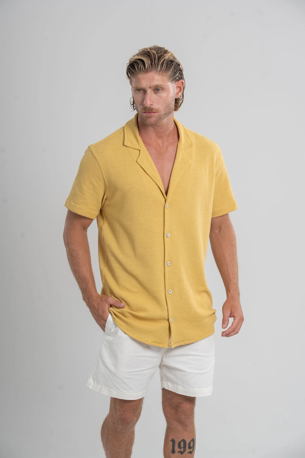 Homem com camisa amarela de manga curta e short off-white