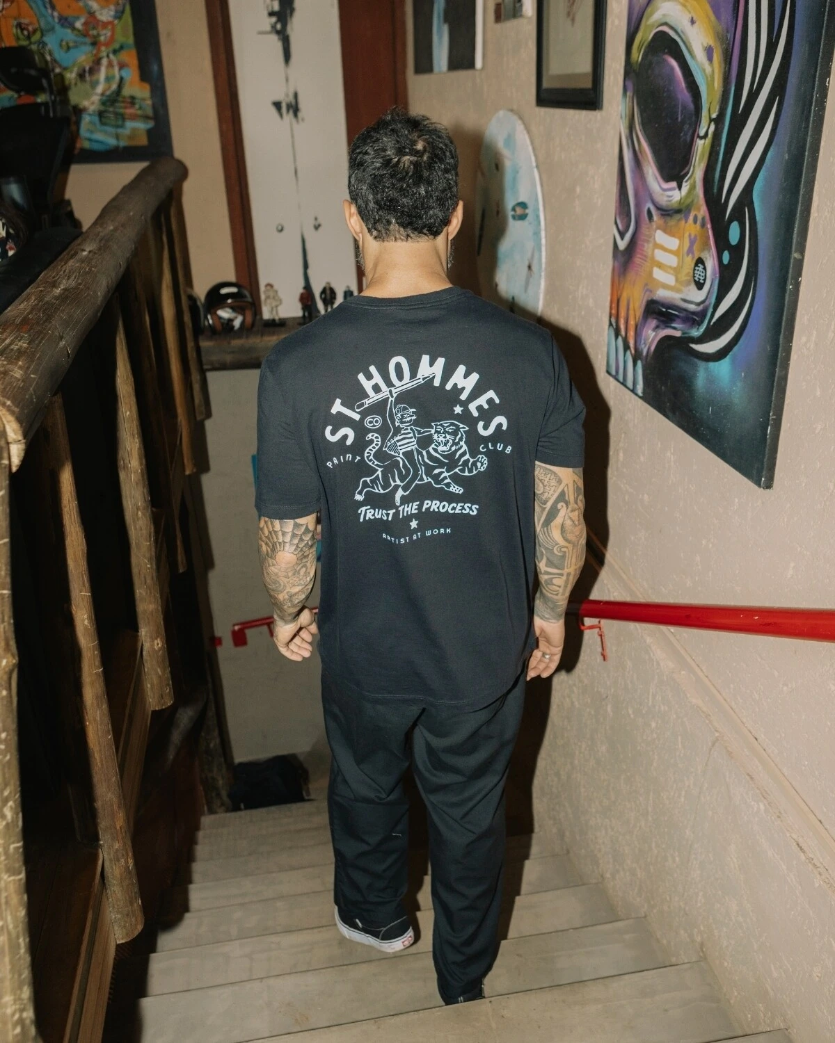 Homem de costas descendo uma escada, vestindo a camiseta St Hommes com a estampa Trust the Process